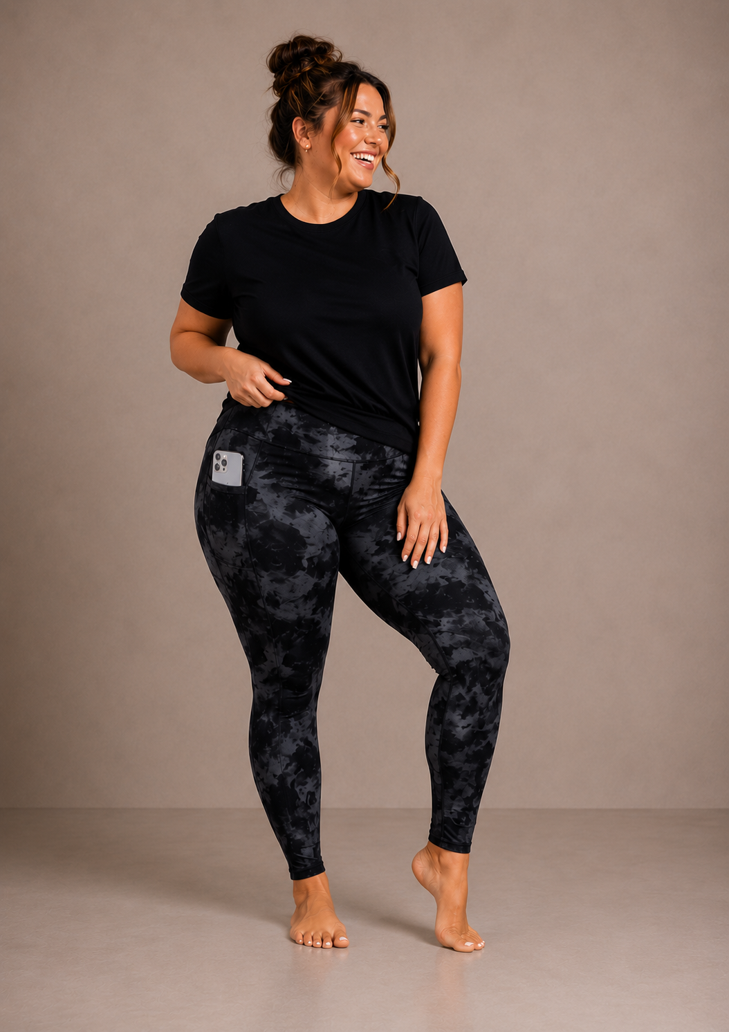 Woman wearing Barefoot & Busy Black Marble high waisted pocket leggings with a black t-shirt in a bright modern studio.