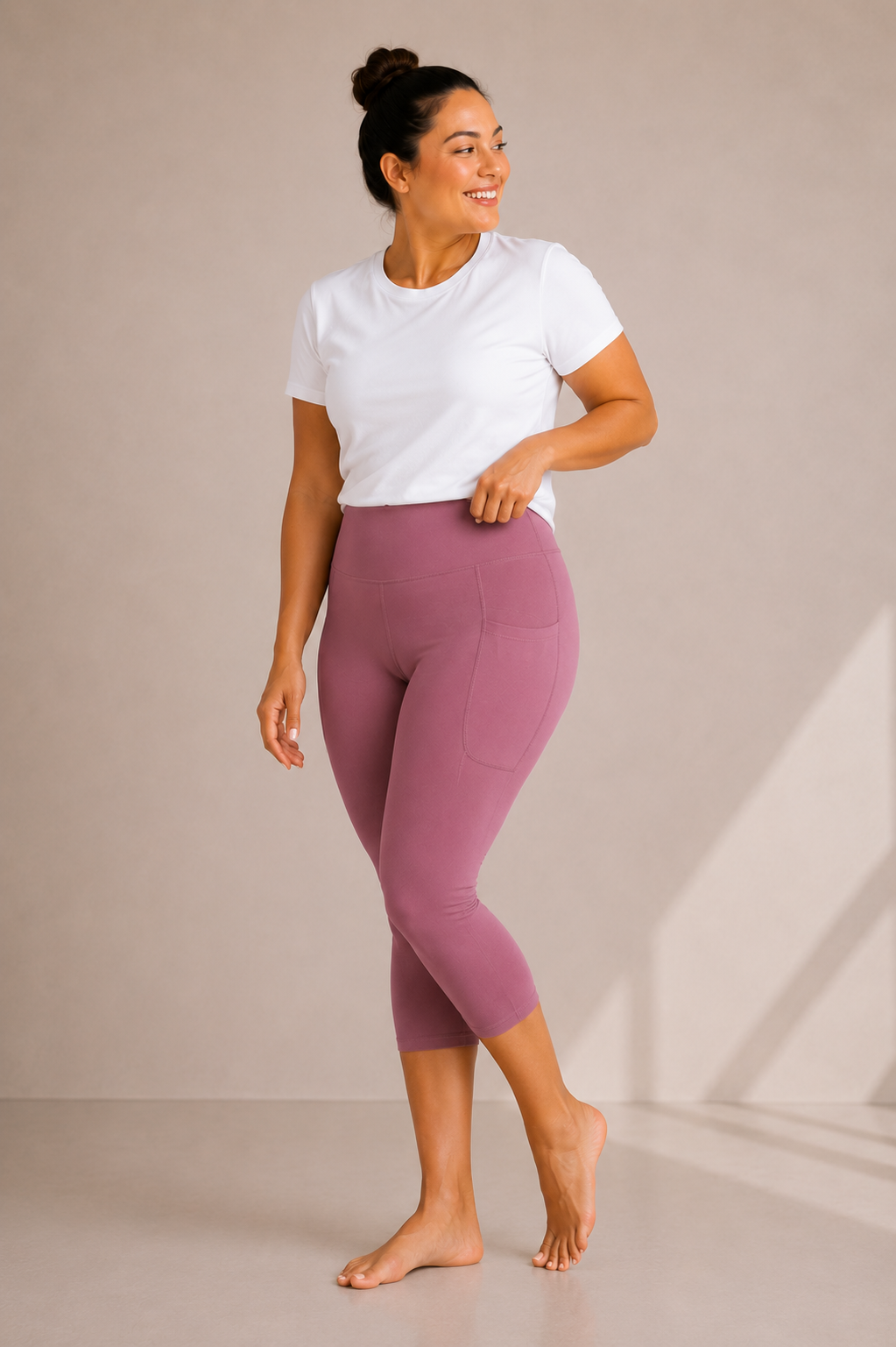 Woman wearing Barefoot & Busy Desert Rose high waisted pocket capri leggings with a white t-shirt in a bright modern studio.