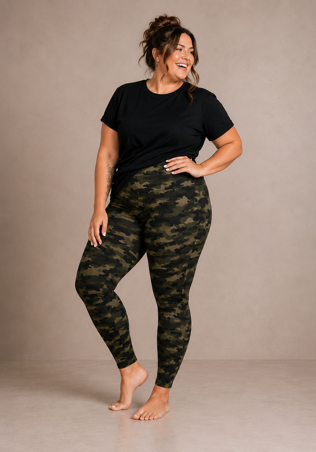 Woman wearing Barefoot & Busy Olive Camo high waisted pocket leggings with a black t-shirt in a bright modern studio.