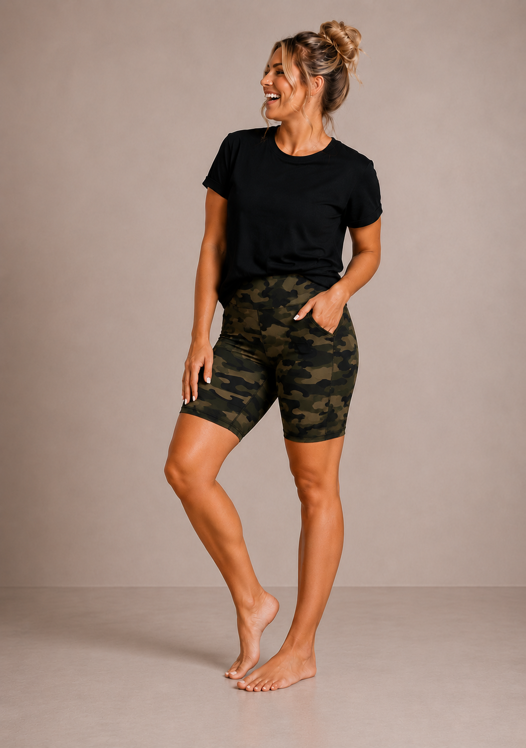 Woman wearing Barefoot & Busy Olive Camo high waisted pocket shorts with a black t-shirt in a bright modern studio.